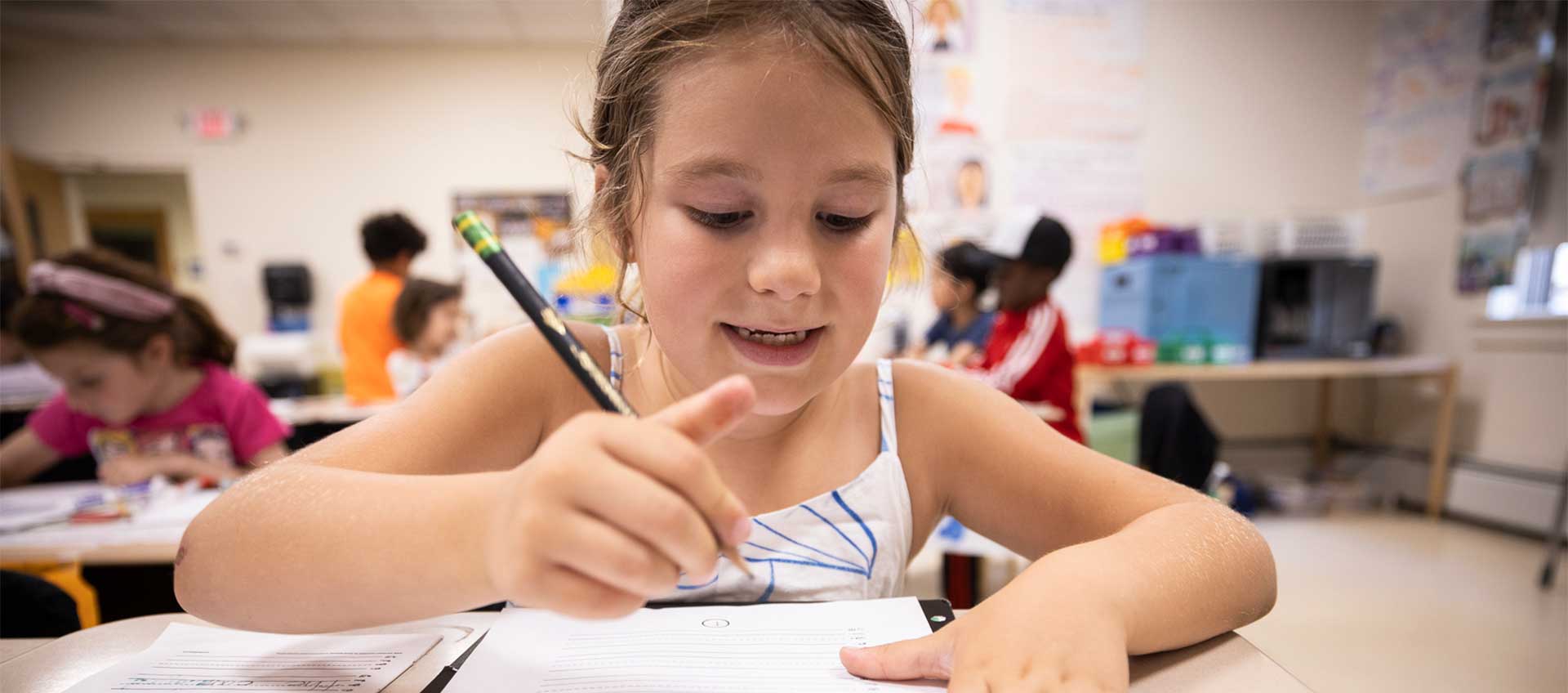 A smiling student writes at her desk.