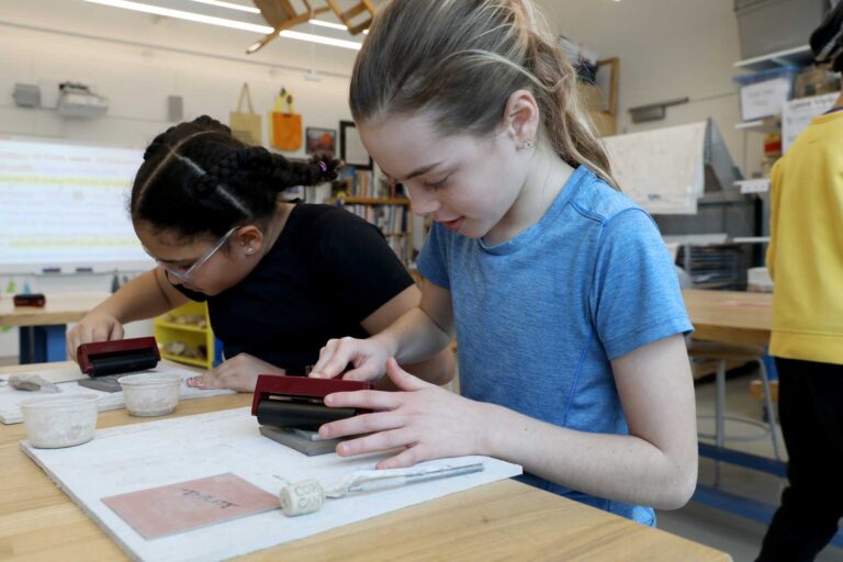 Two students roll clay for their vessels