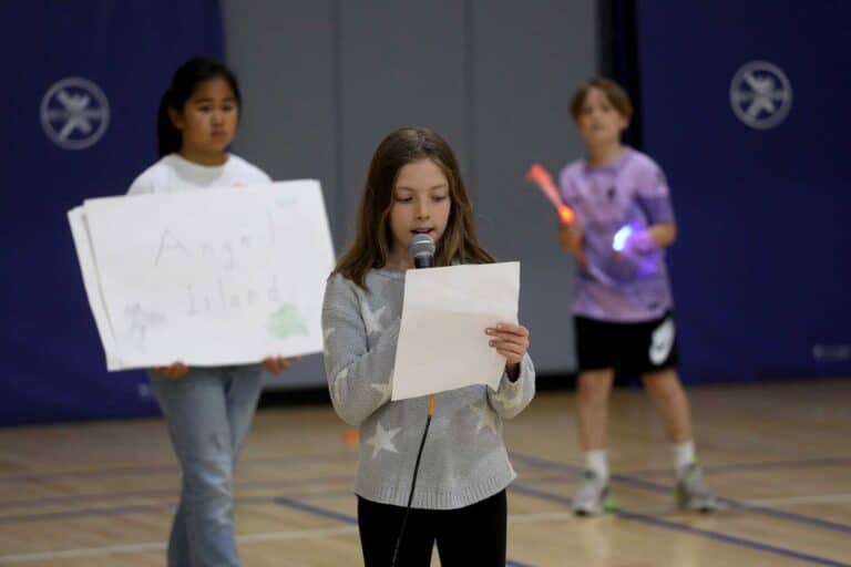 Three students presenting, one holding a microphone and another holds a poster