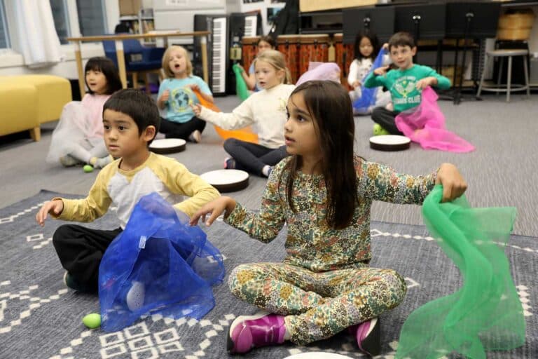 Students sit cross-legged and sing a song in French class