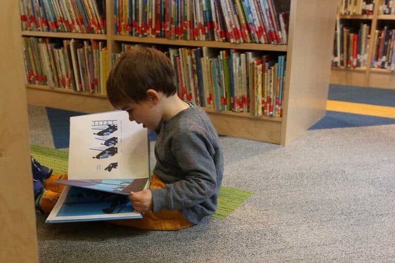 A student sits on the library floor with a picture book