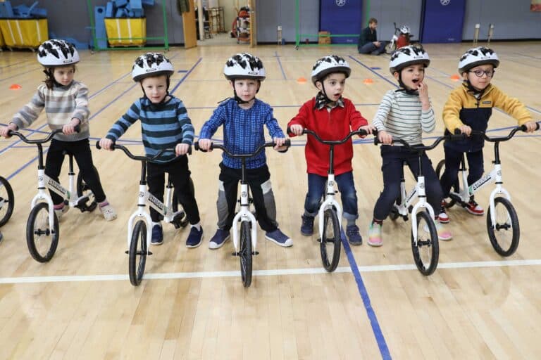 Six pre-k students on balance bikes in the gym
