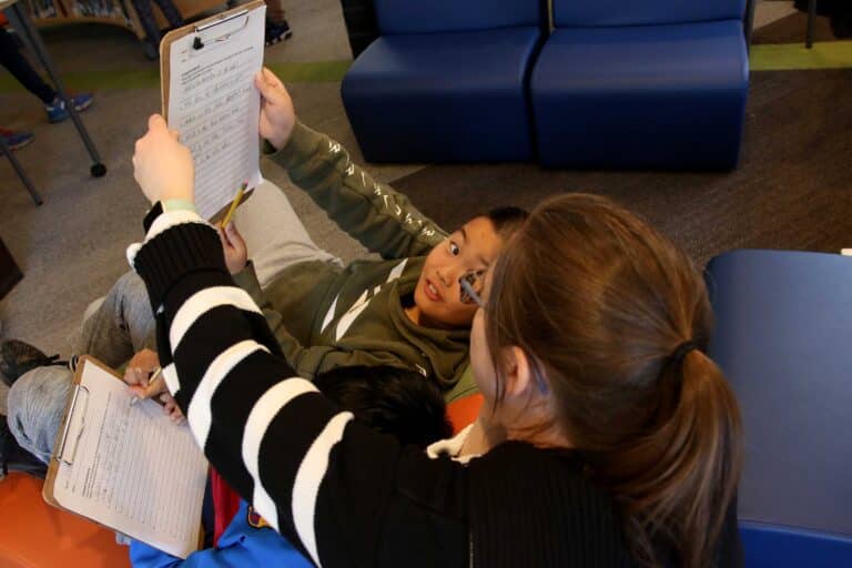 Two students compare notes on clipboards