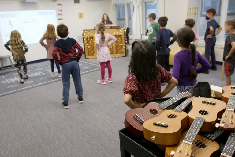 A view of the music room and ukuleles with students facing the teacher and singing