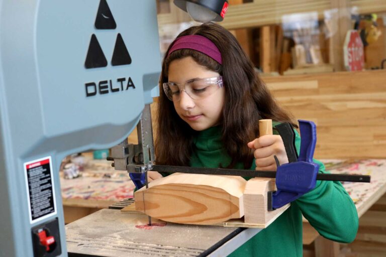 A girl works with a table saw in the woodworking studio