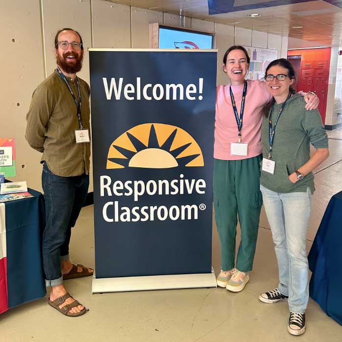 Three teachers stand with a sign that says "Welcome! Responsive Classroom"