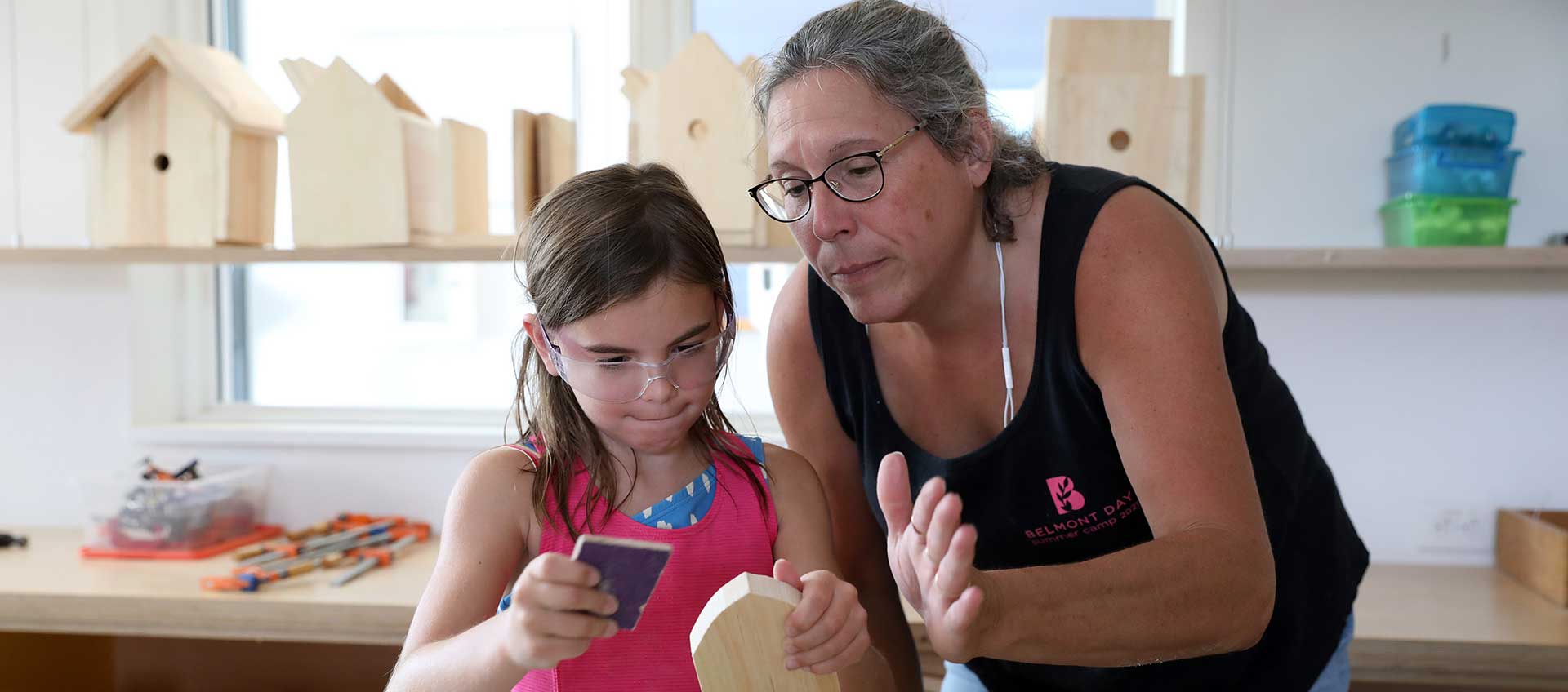 A camper and counselor side by side working in the woodworking studio