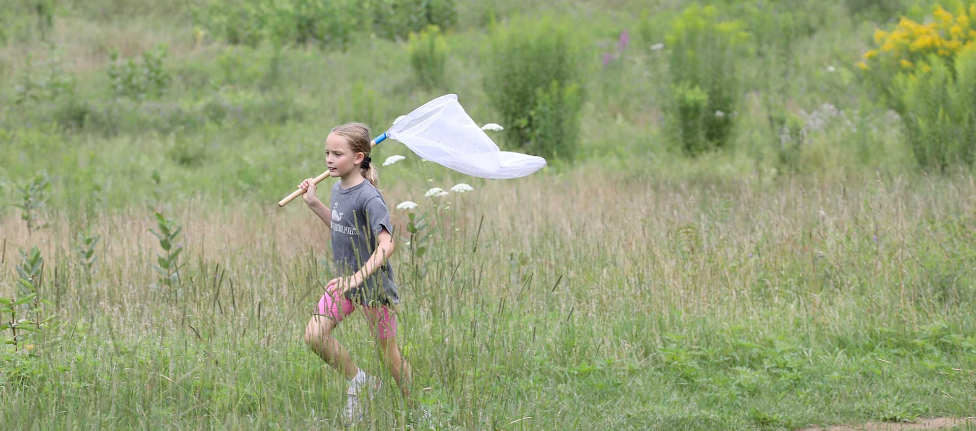 A camper runs through a meadow with a butterfly net